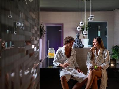 Zwei Personen in Bademänteln sitzen an einer Bar in einem modernen Wellnessbereich.