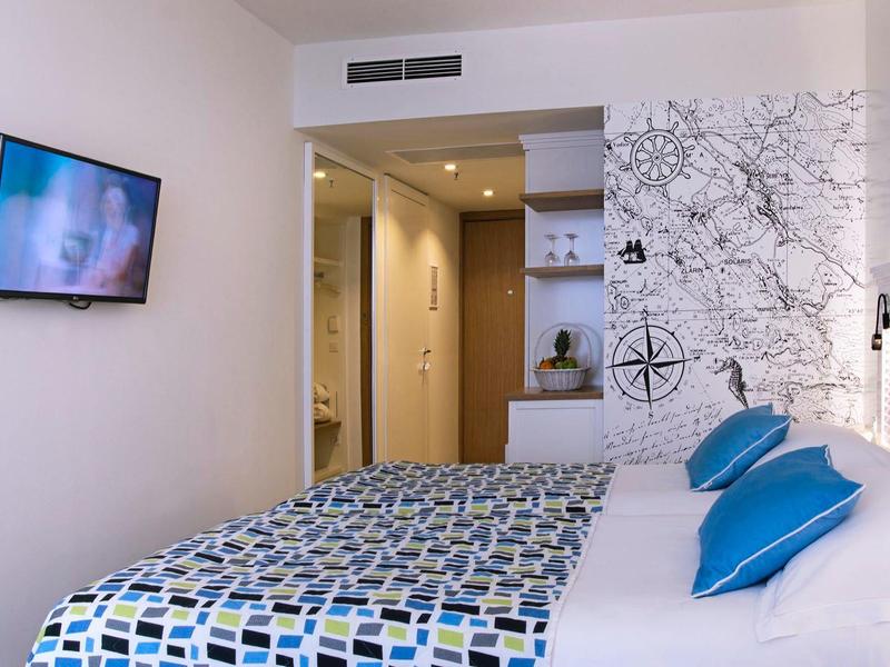 Modernes Hotelzimmer mit Doppelbett, buntem Bettbezug und Wandbild hinter dem Bett.