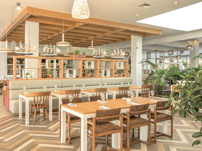 Helles, modernes Restaurant mit Holztischen, Stühlen und grünen Pflanzen.