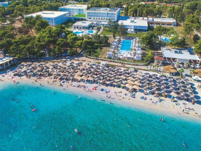 Strandresort mit vielen Sonnenschirmen am türkisfarbenen Meer und mehreren Pools im Hintergrund.