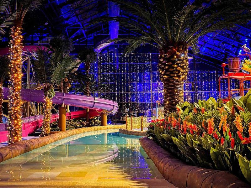 Innenpool mit Palmen, farbiger Beleuchtung und üppigen Pflanzen im Hotel-Resort.