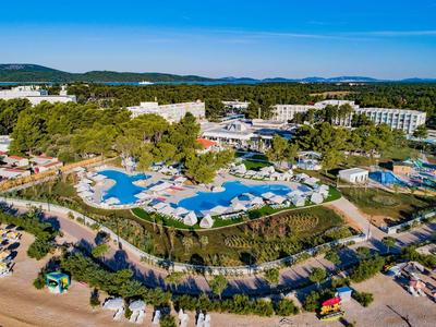 Groot hotelresort met meerdere zwembaden, ligstoelen en omgeven door groen landschap.