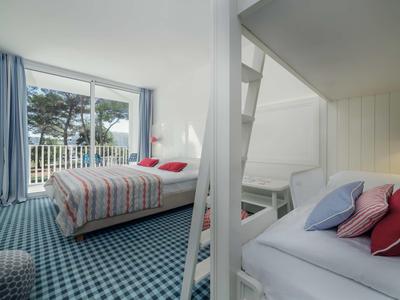 Lichte hotelkamer met tweepersoonsbed, stapelbed en balkon uitzicht met bomen.