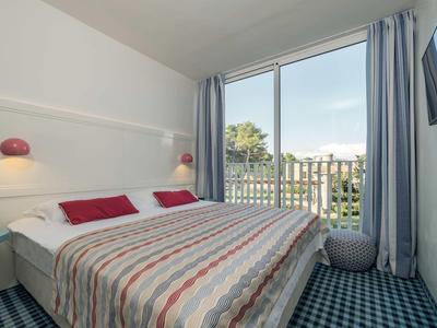 Lichte hotelkamer met tweepersoonsbed en balkon met uitzicht op bomen en stad.