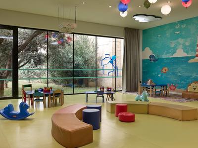 Sala de juegos infantil con mesas, asientos y mural con faro y mar