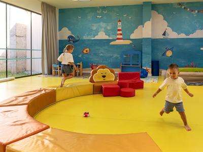 Área de juegos para niños iluminada con grandes ventanas, elementos para trepar y asientos.