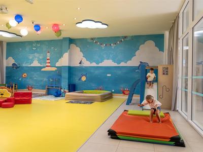 Sala de juegos infantil colorida con colchonetas suaves, muro de escalada y diseño de nubes en la pared.