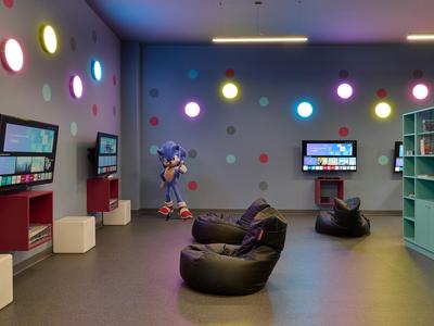 Sala de juegos colorida con pufs, televisores montados y círculos luminosos en las paredes.