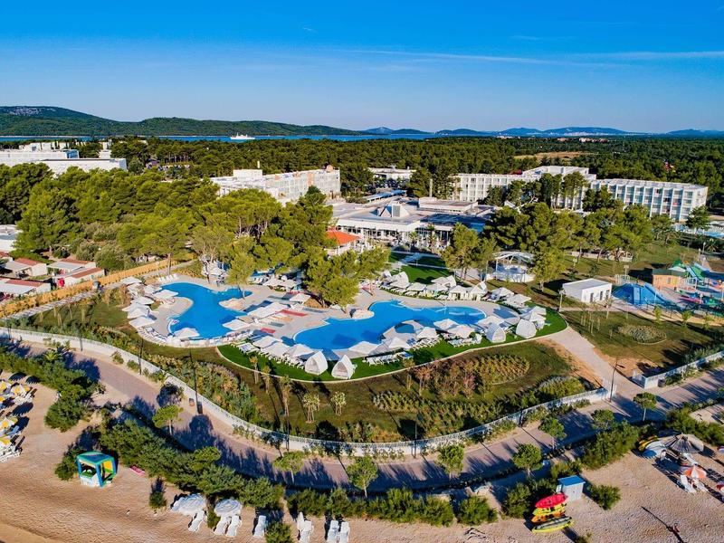 Groot hotelresort met meerdere zwembaden, ligstoelen en omgeven door groen landschap.