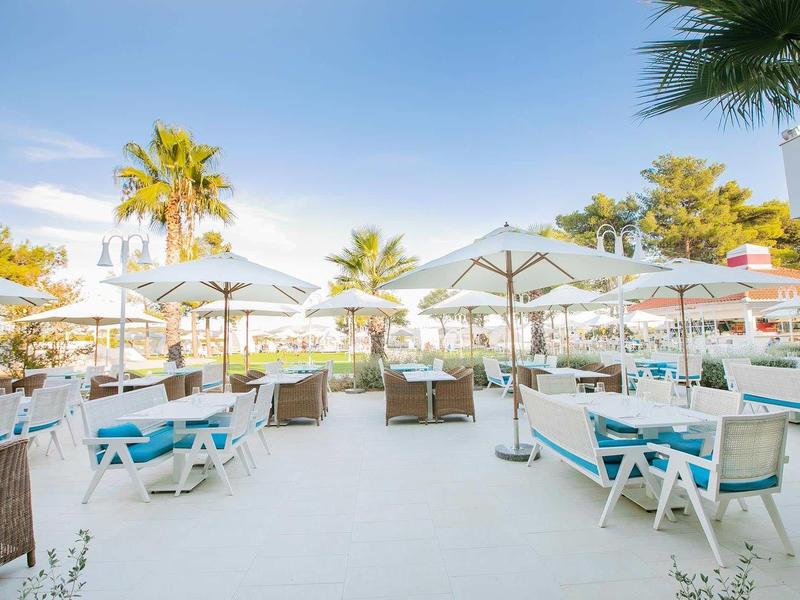 Strandrestaurant met witte tafels en stoelen onder parasols bij palmbomen