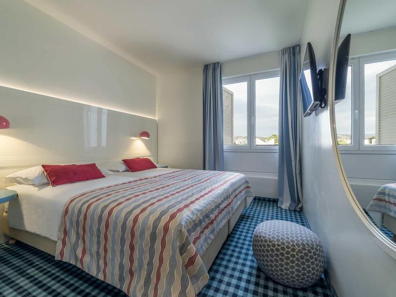 Lichte hotelkamer met tweepersoonsbed, blauwe gordijnen en spiegel aan de muur.