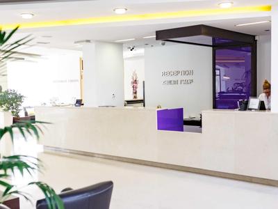 Moderner Hotel-Empfang mit weißem Tresen und lila Akzenten in hellem Raum.