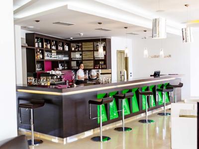 Moderner Hotelbarbereich mit grünen Barhockern und dunklem Holzthekenbereich.