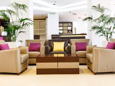 Helle Hotellobby mit beigefarbenen Sofas, bunten Kissen und grünen Pflanzen.