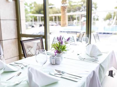 Eleganter gedeckter Tisch mit weißer Tischdecke und Blumendekor vor großen Fenstern.