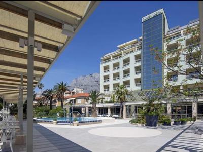 Modernes Hotelgebäude mit Swimmingpool und Sitzbereich unter blauem Himmel.
