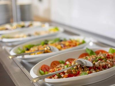 Mehrere weiße Schüsseln mit verschiedenen frischen Salaten auf einem Buffet.