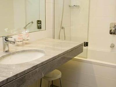 Modernes Badezimmer mit Waschbecken, Spiegel, Hocker und Badewanne mit Glasduschabtrennung.