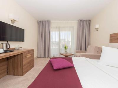 Modernes Hotelzimmer mit großem Bett, Flachbildfernseher, Holzmöbeln und Fenster mit grauen Vorhängen.