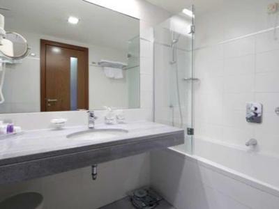 Weißes Badezimmer mit Wandspiegel, Waschbecken, Haartrockner und Badewanne mit Duschvorhang.