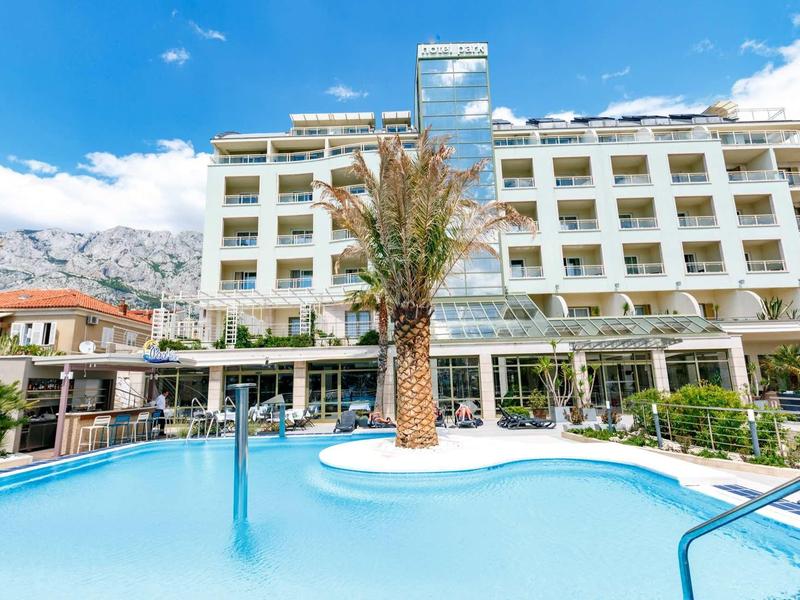 Moderner mehrstöckiger Hotelbau mit großem Pool und Palme in klarem blauem Himmel.