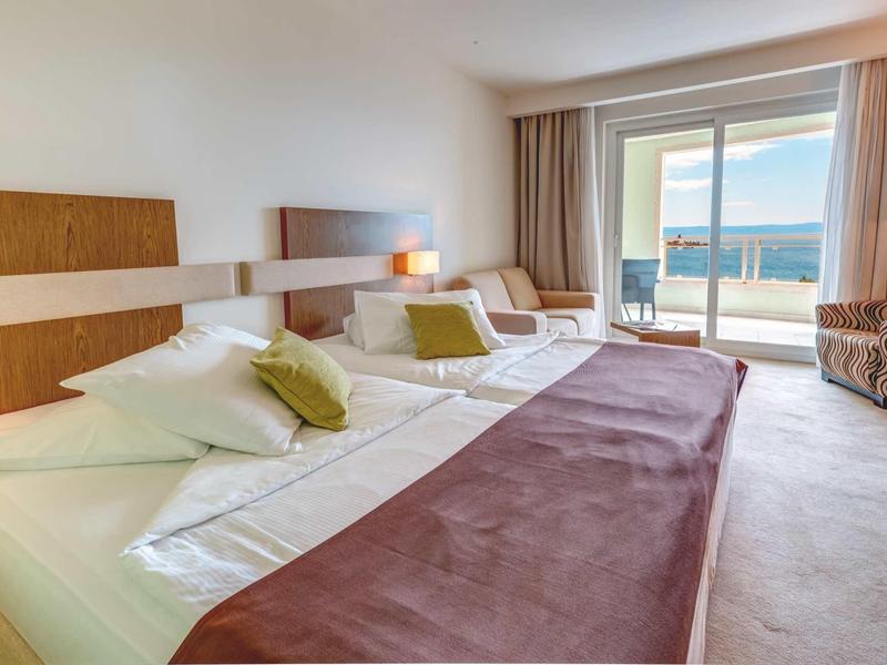 Helles Hotelzimmer mit zwei Betten, braunen Kopfstützen, großem Fenster und Meerblick.