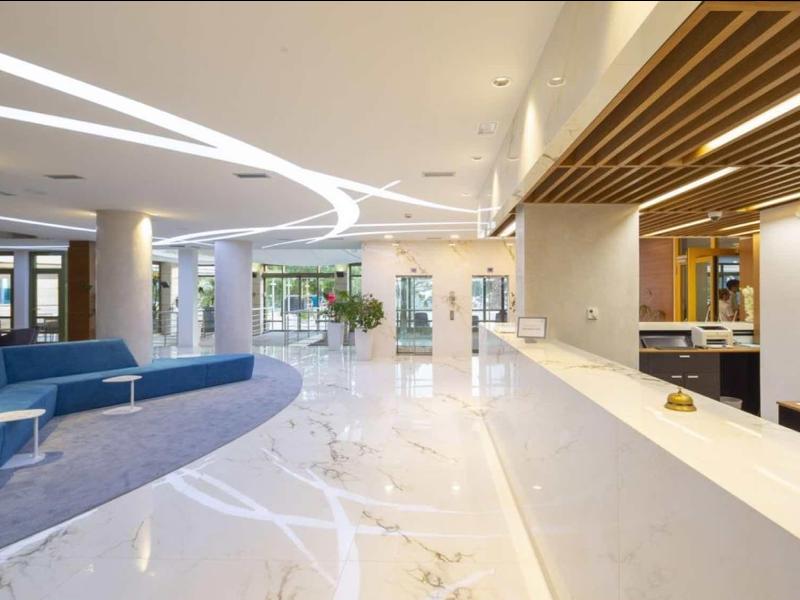 Großer, heller Hotel-Lobby mit glänzendem Marmorfußboden, blauen Sofas und moderner Empfangstheke.