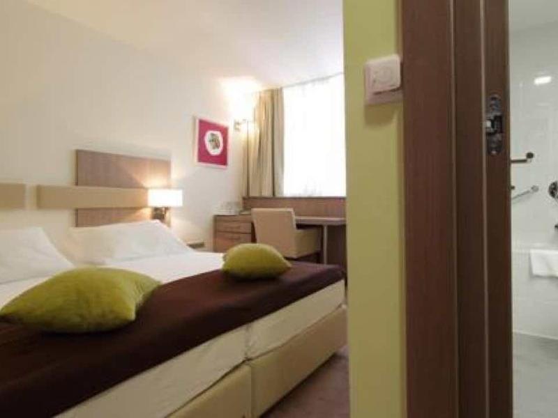 Helles, modernes Hotelzimmer mit Doppelbett, weißen Wänden, Holzmöbeln und angrenzendem Bad.