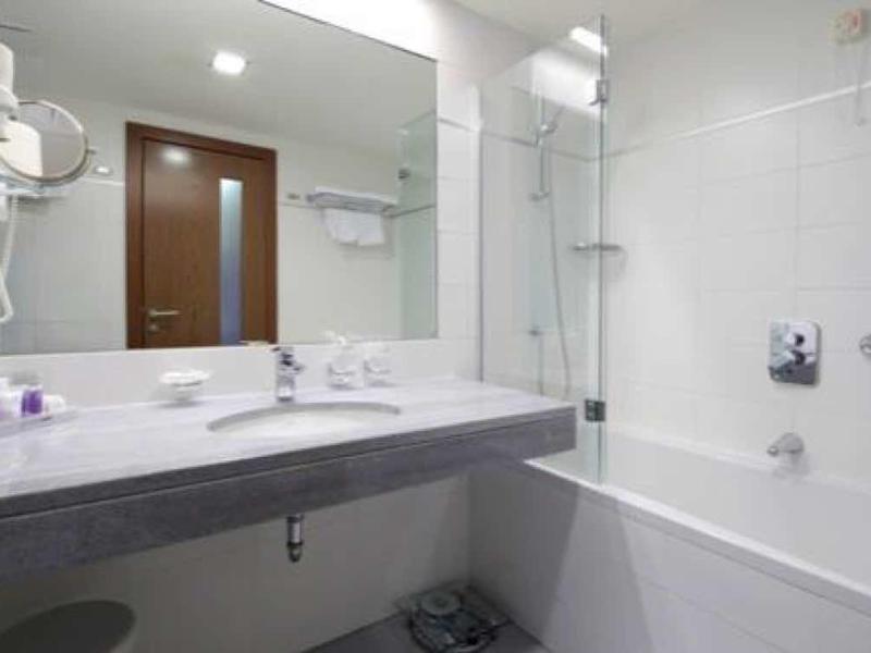 Weißes Badezimmer mit Wandspiegel, Waschbecken, Haartrockner und Badewanne mit Duschvorhang.