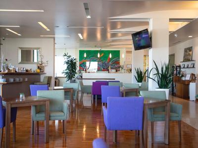 Nowoczesna restauracja hotelowa z kolorowymi krzesłami, drewnianą podłogą, roślinami i jasnym oświetleniem.