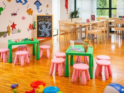 Kolorowy pokój zabaw dla dzieci z małymi stolikami, różowymi stołkami i dekoracjami na ścianach w jasnym pomieszczeniu.