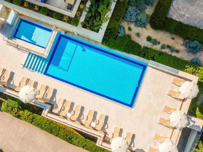 Vista aerea di una piscina rettangolare blu all'aperto con lettini e ombrelloni su una terrazza.