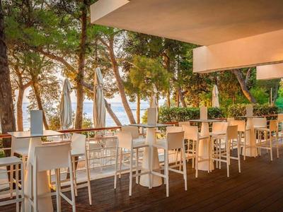 Terras met witte stoelen en tafels onder bomen met uitzicht op zee bij zonsondergang