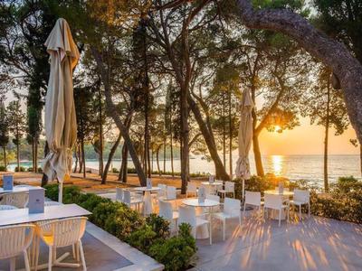 Buitenrestaurant met witte tafels en stoelen bij zonsondergang aan het water.