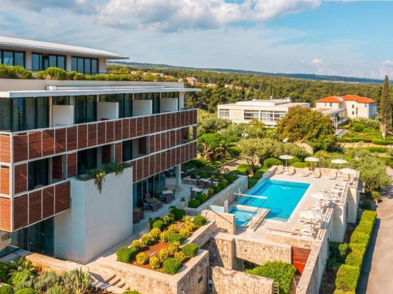 Nowoczesny kompleks hotelowy z basenem na zewnątrz i przestronnymi tarasami w zielonym otoczeniu.