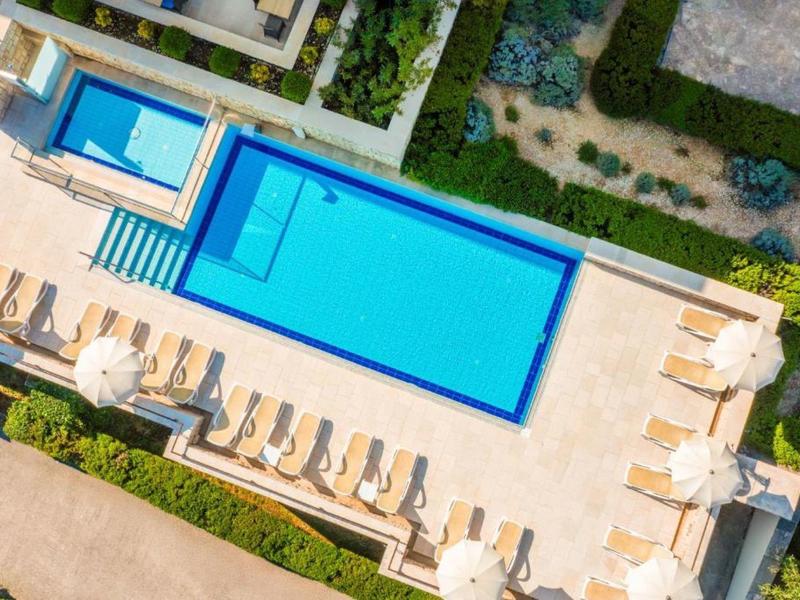Widok z lotu ptaka na prostokątny, niebieski basen na zewnątrz z leżakami i parasolami na tarasie.