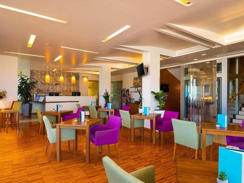 Nowoczesna, jasna restauracja z drewnianą podłogą, kolorowymi krzesłami i subtelną atmosferą.