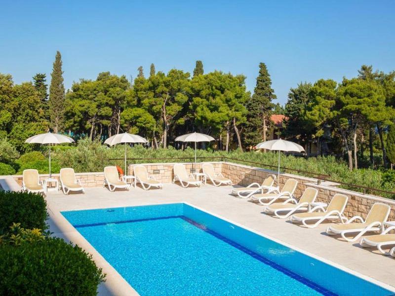 Ogrzewany basen na świeżym powietrzu z leżakami i parasolami otoczony drzewami.