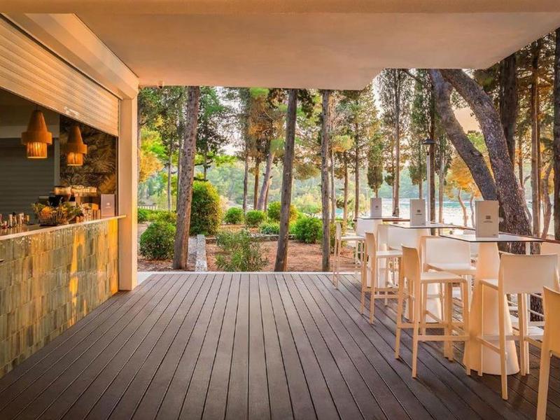 Otwarta przestrzeń z barem i białymi krzesłami z widokiem na las i morze.