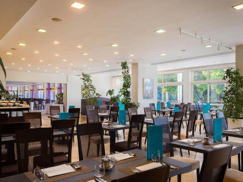 Nowoczesna restauracja z ciemnobrązowymi krzesłami, stolikami i dużymi oknami z widokiem na zieleń.