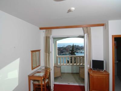 Kleines Hotelzimmer mit Schreibtisch, Stuhl, Fernseher und Balkon mit Blick auf die Stadt.