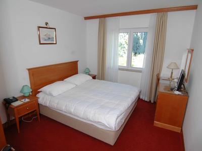 Kleines Hotelzimmer mit Doppelbett, roten Teppichboden und hellen Vorhängen