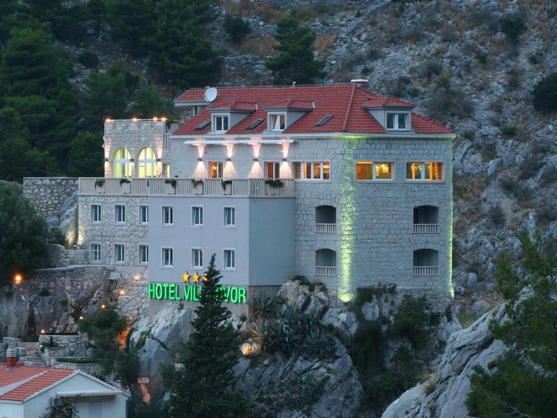 Großes mehrstöckiges Hotel mit roten Dachziegeln in felsiger Berglandschaft bei Dämmerung.