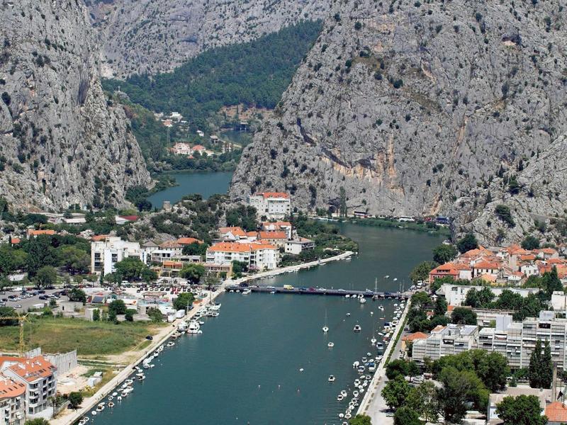Berglandschaft mit Fluss, Brücke und Ortschaft am Ufer, umgeben von steilen Felsen.