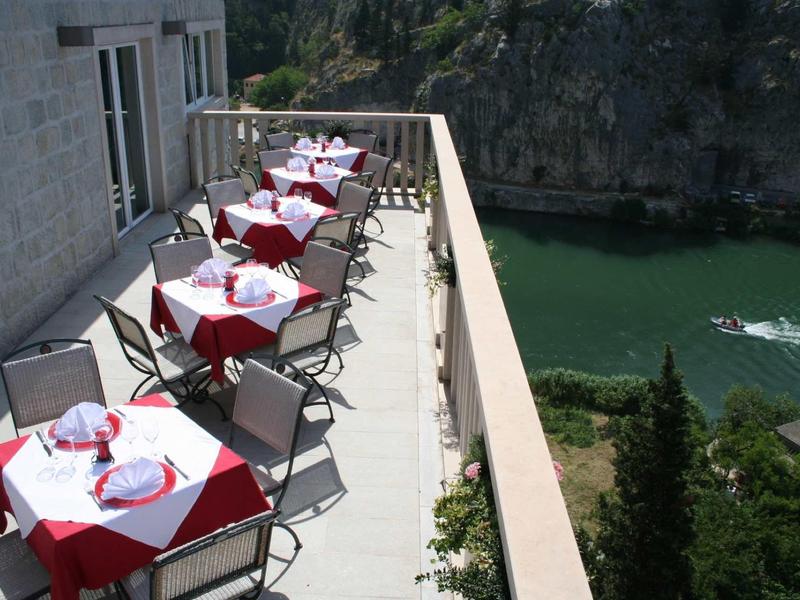 Balkon mit geschmückten Tischen und Stühlen neben Felsen und grünem Wasser unter klarem Himmel.