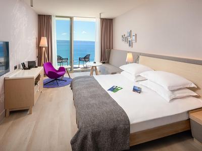 Modernes Hotelzimmer mit Doppelbett, Meerblick, Sitzecke und Fernseher.