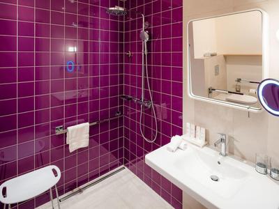 Modernes Badezimmer mit glänzenden lila Fliesen, Duschkabine und weißem Waschbecken.