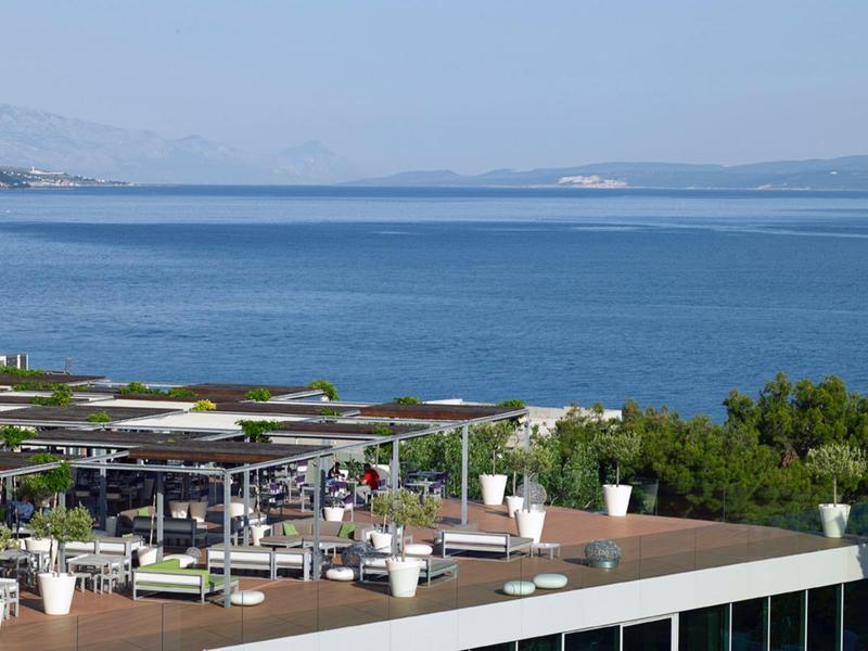 Terrazza sul tetto con aree salotto che si affacciano sul mare blu e montagne lontane.