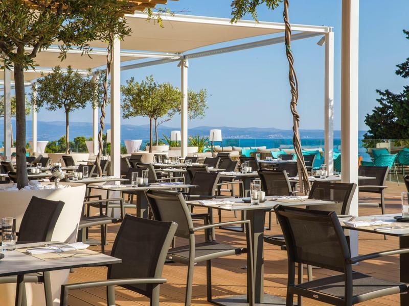 Area esterna di un ristorante vuota con vista sul mare e posti a sedere sotto tende bianche.