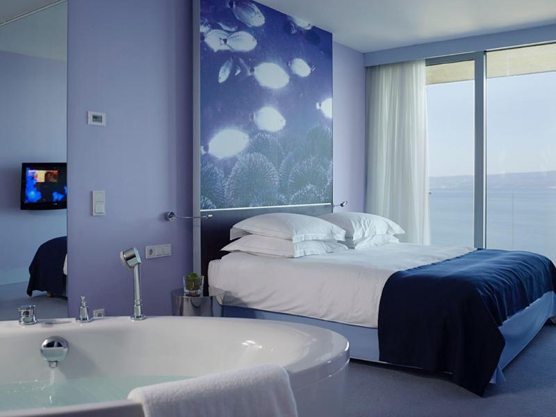 Camera d'hotel moderna con letto matrimoniale, decorazione murale blu e vista mare da grandi finestre.
